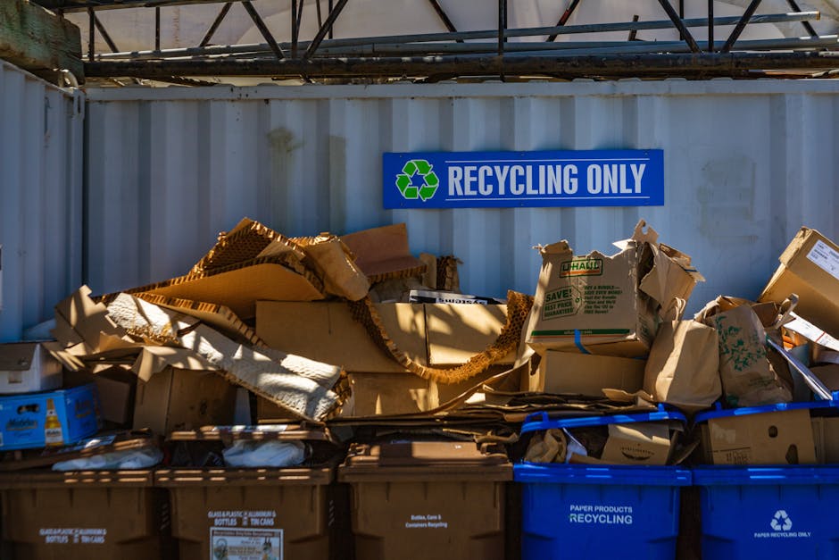A large heap of assorted scrap metal and discarded household items, including rusted pipes, metal rods, and broken furniture, all piled together in an outdoor yard or storage area. The metals vary in 